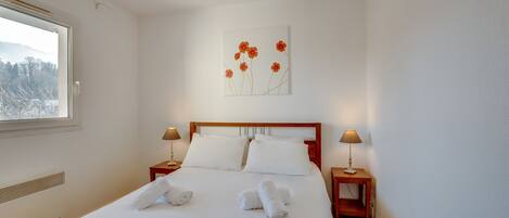 A neatly made bed with white linens and towels, a wooden headboard, two bedside tables with lamps, and a wall-mounted artwork of flowers.