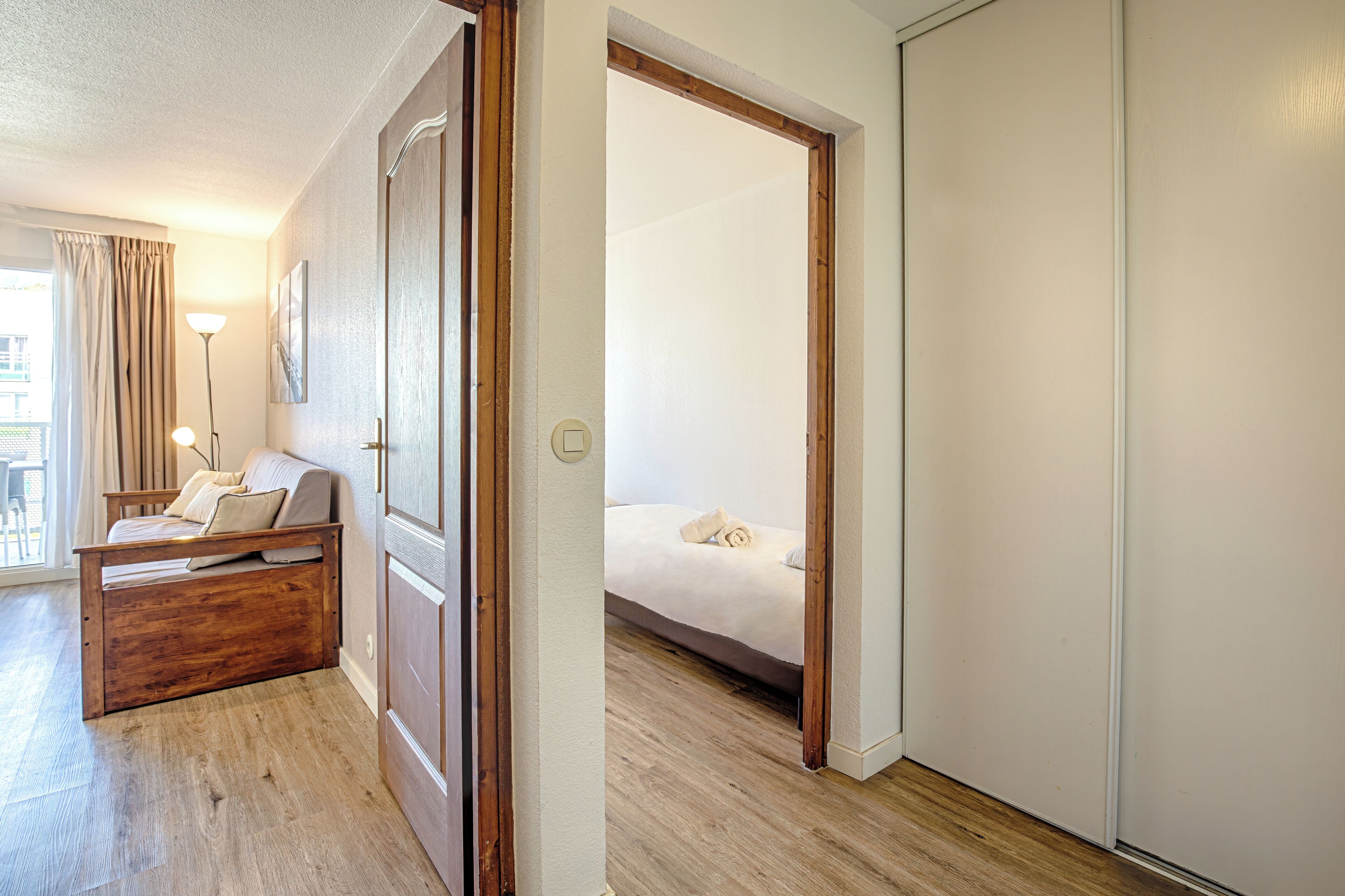 A hotel room with a wooden bed, a sofa, a lamp, and a view of the outside.