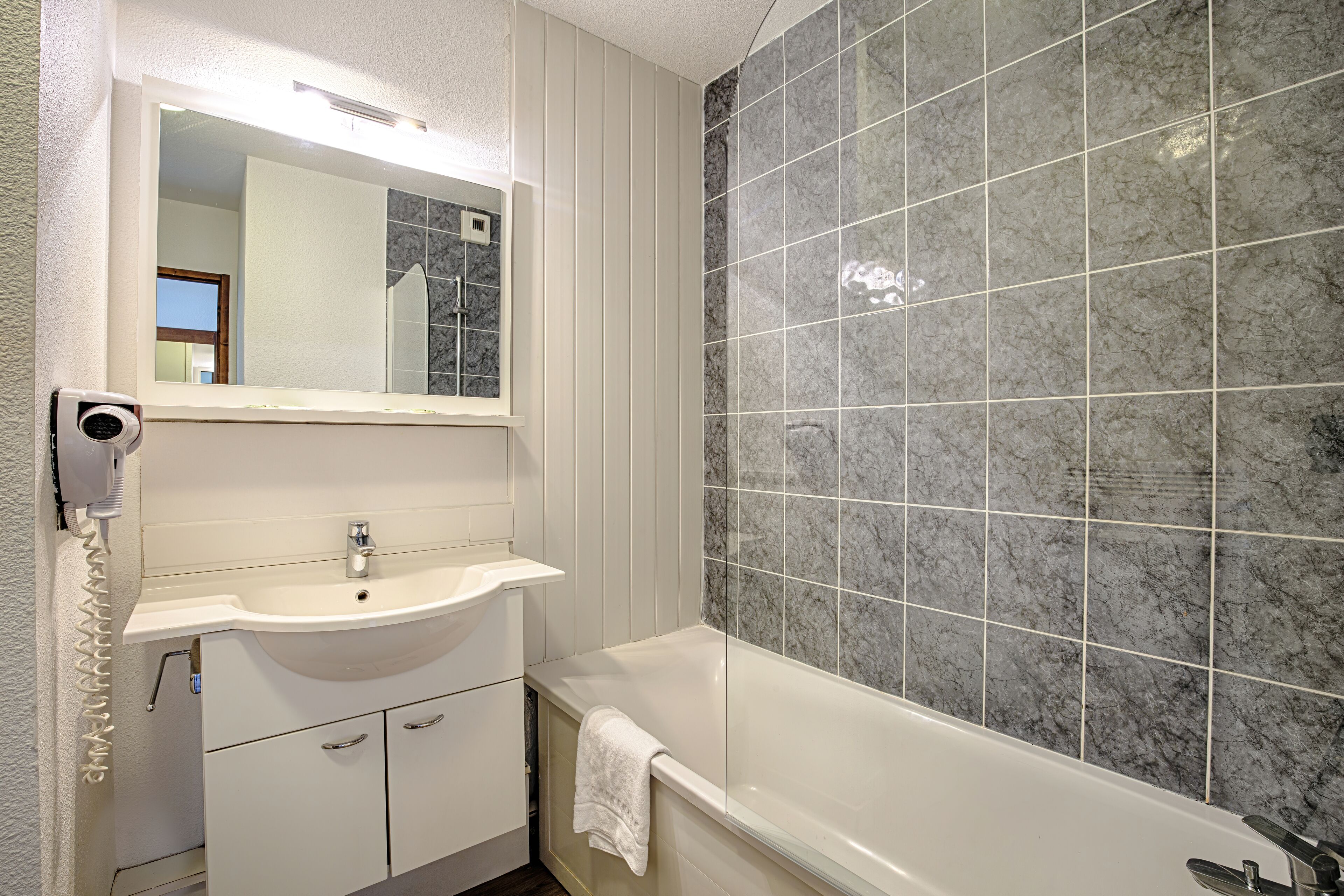 A bathroom with a white sink, mirror, and bathtub.