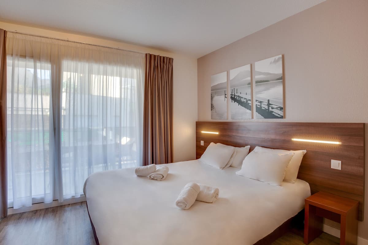 Una cama bien tendida con sábanas blancas y dos toallas enrolladas, un cabecero de madera y una mesita de noche.