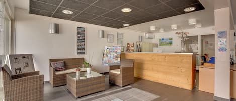 Un espace d'accueil aménagé avec des meubles en osier, un comptoir d'accueil en bois et un panneau d'affichage où sont accrochées des annonces.
