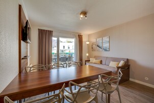Un comedor moderno con una mesa de madera y sillas blancas, un sofá y un televisor montado en la pared.