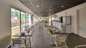 A spacious dining area with tables and chairs, a kitchen area with appliances, and large windows providing natural light. - ResidHotel Azuréa (Aix-les-Bains)