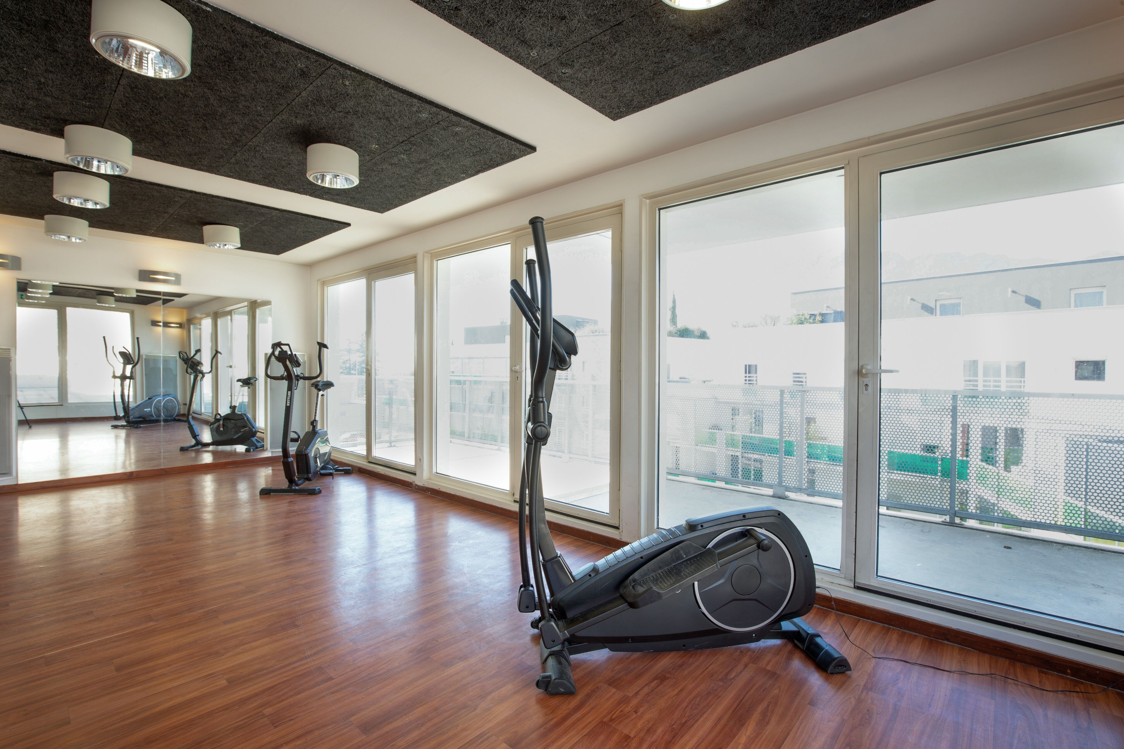 A spacious gym with large windows, wooden floors, and various exercise equipment.
