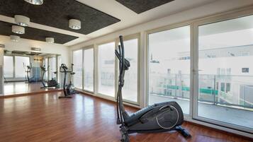 A spacious gym with large windows, wooden floors, and various exercise equipment.