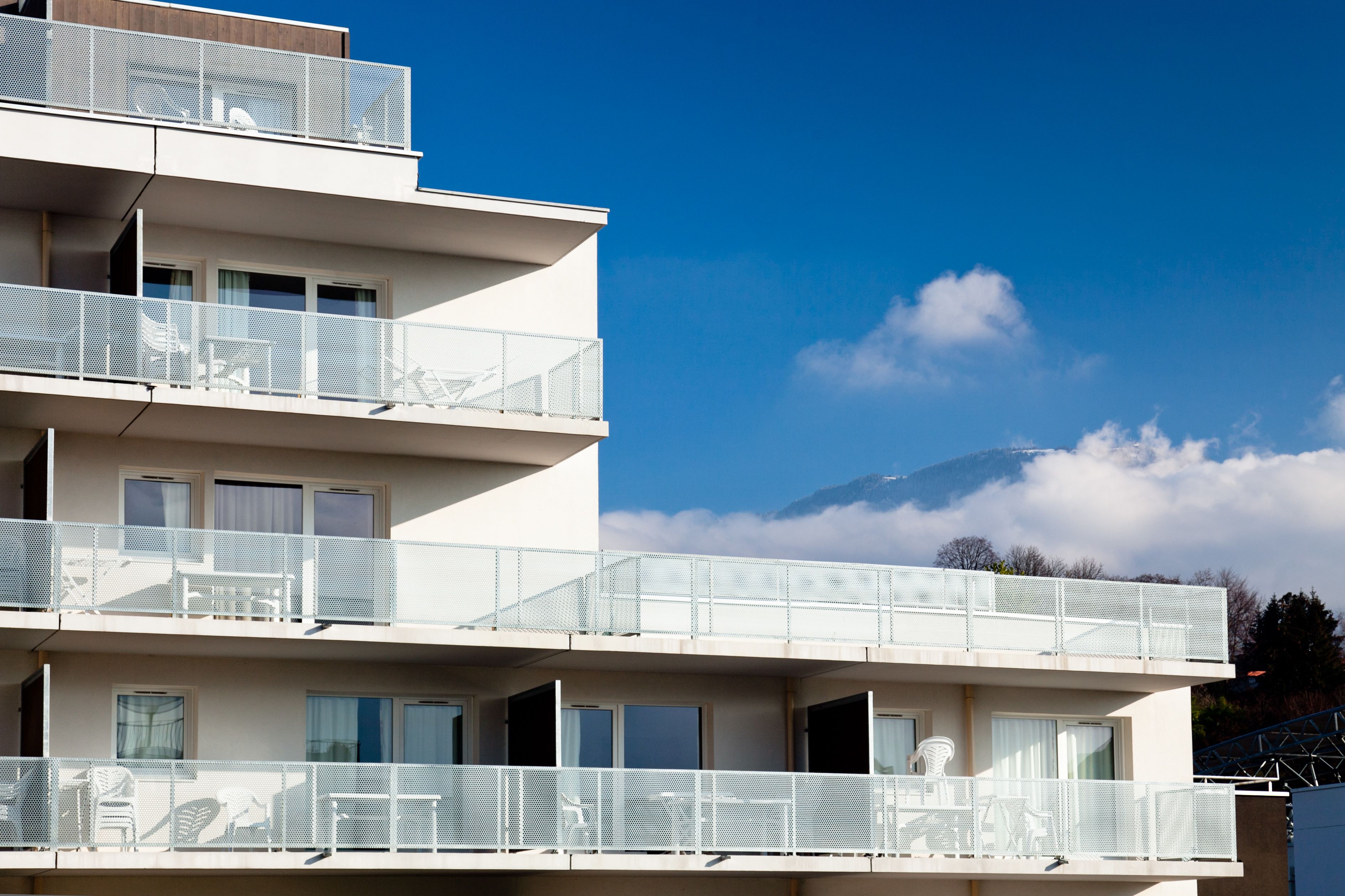 A multi-story building with balconies, large windows, and a view of a mountain.