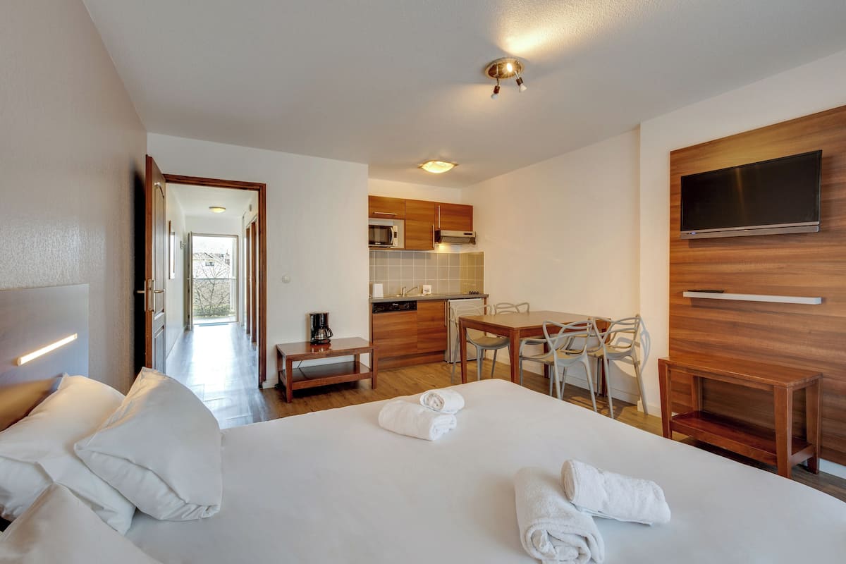 Una habitación de hotel con cama, escritorio, silla, televisor y kitchenette.