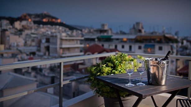 A balcony with a table, two wine glasses, and a bottle of champagne in a bucket. - Areos Hotel (Athens)