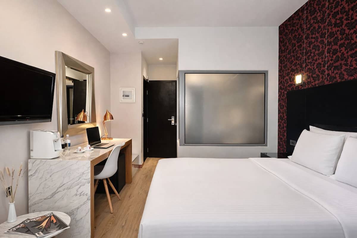 Une chambre d’hôtel avec un lit, un bureau avec un ordinateur portable, une télévision et une grande fenêtre.