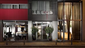 A modern building with a red facade, a glass entrance, and the name 'AREHOS' displayed above the doors. - Areos Hotel (Athens)