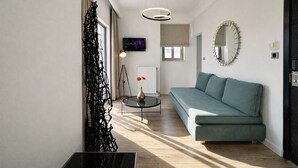 A modern living room with a sofa, a round coffee table, a floor lamp, and a wall-mounted TV. - Areos Hotel (Athens)