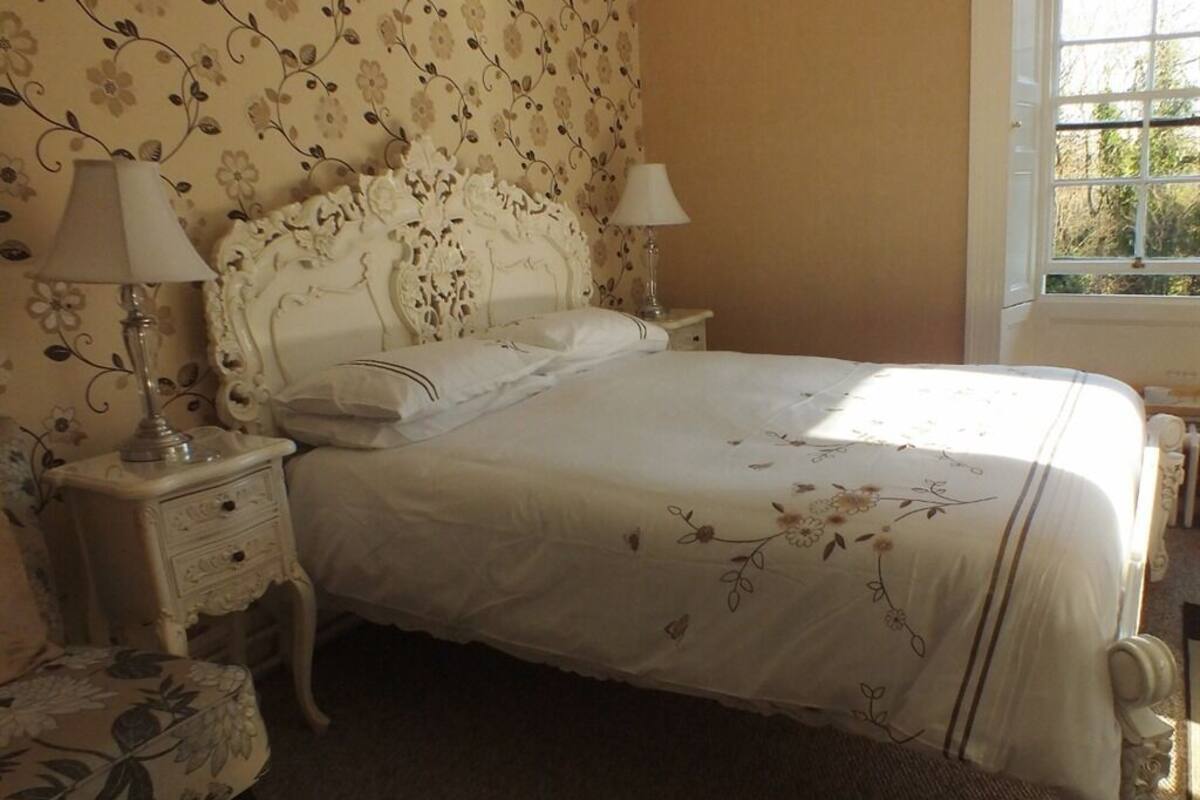 Een netjes opgemaakt bed met bloemenbedrukking, twee nachtkastjes met lampen en een fauteuil met bloemenprint.