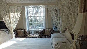 A bedroom with a large bed, two bedside tables, a nightstand, a lamp, and a window with lace curtains. - Hedgefield House Hotel (Blaydon on Tyne)