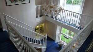 A high-ceilinged room with a chandelier, a staircase, and a large window offering a view of greenery. - Hedgefield House Hotel (Blaydon on Tyne)