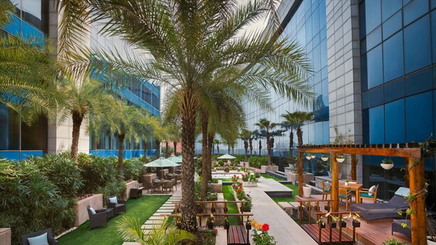 A courtyard with palm trees, outdoor seating, and a pergola. - The Leela Ambience Gurugram Hotel & Residences - The Luxury Urban Sanctuary (Gurugram)