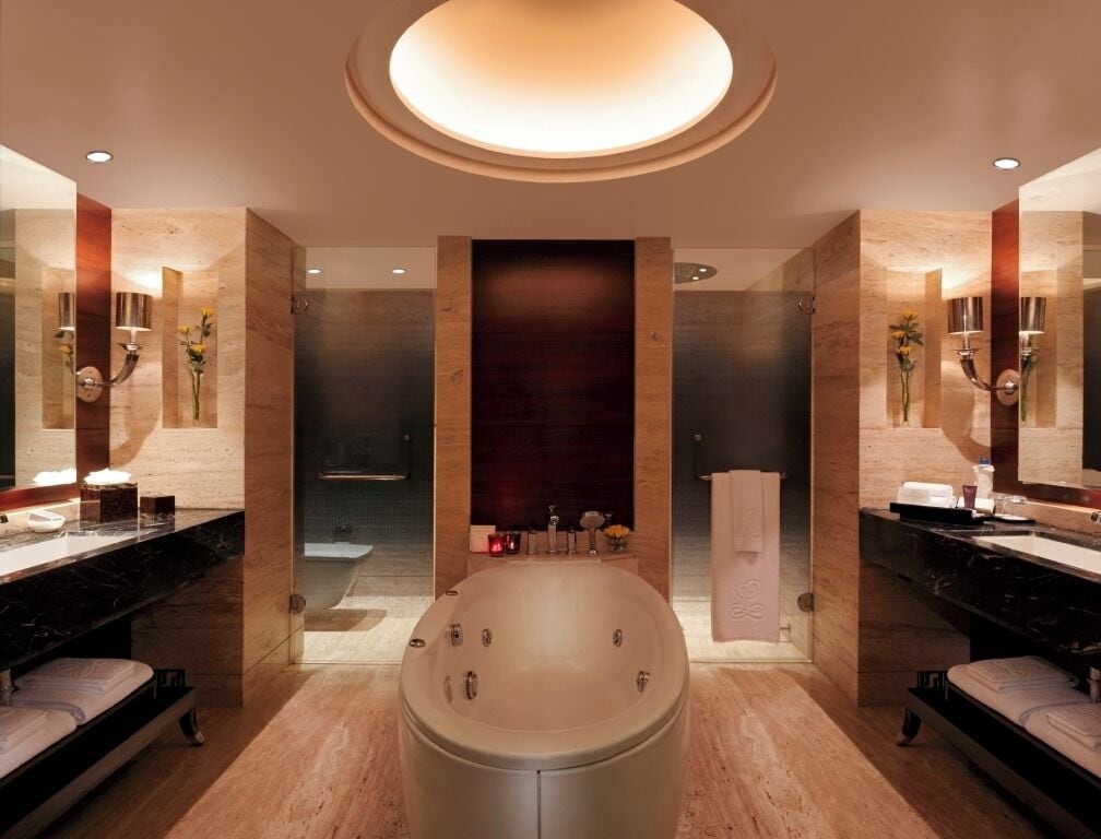 A modern bathroom with a central bathtub, two sinks, and a large mirror.