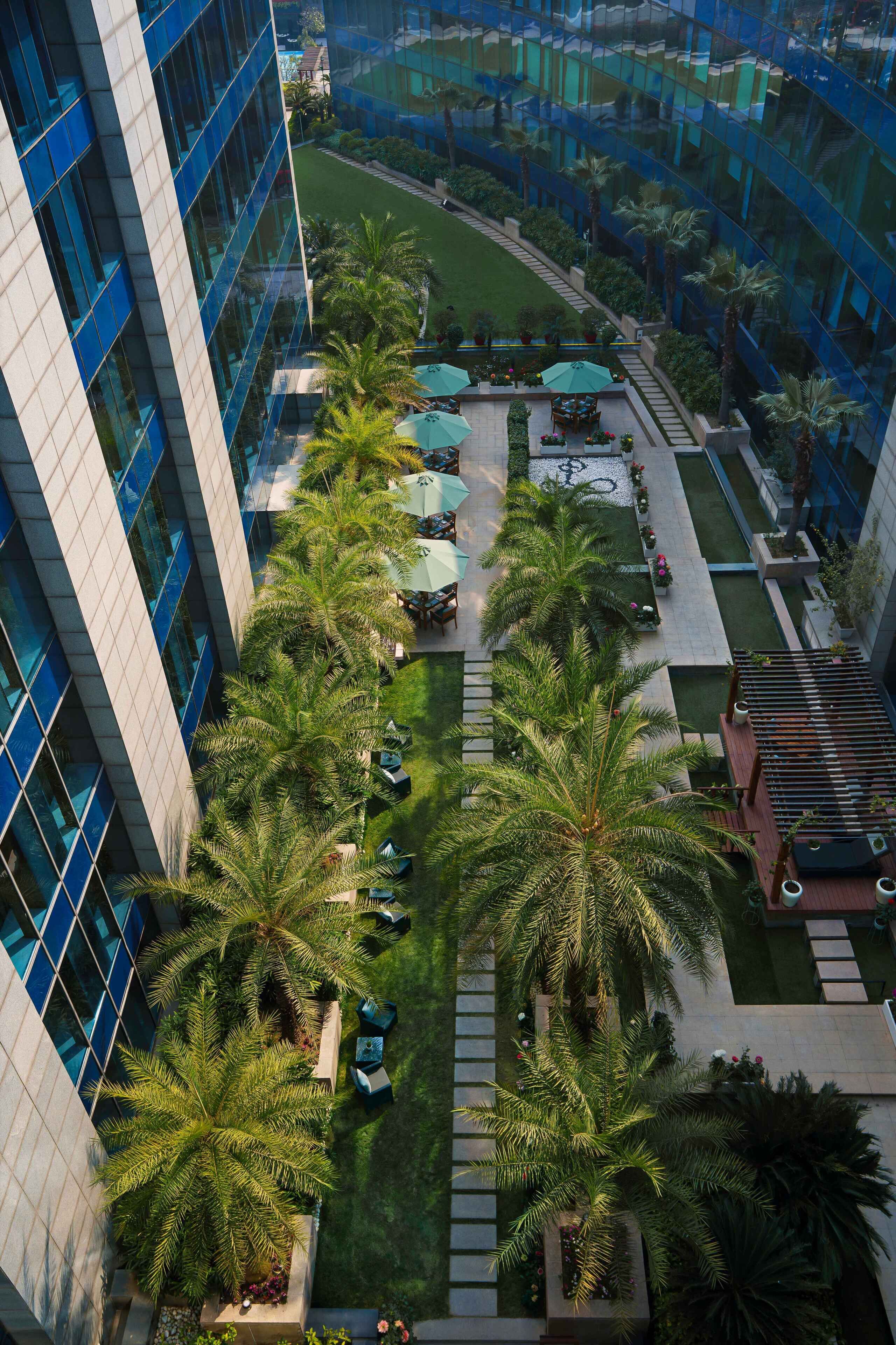 Un edificio moderno con fachada de vidrio curva, un patio central con palmeras, mobiliario exterior y una zona de piscina.