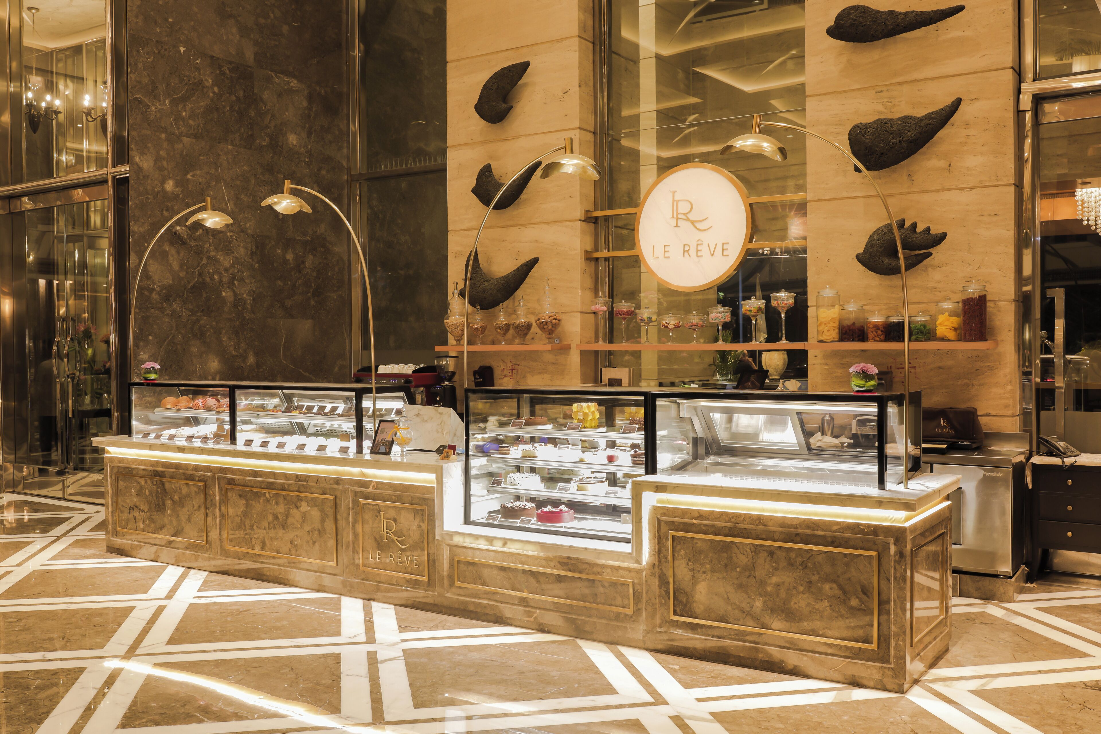 Un présentoir à desserts avec un sol en marbre, une vitrine contenant divers desserts et une enseigne portant le logo « Le Réve ».