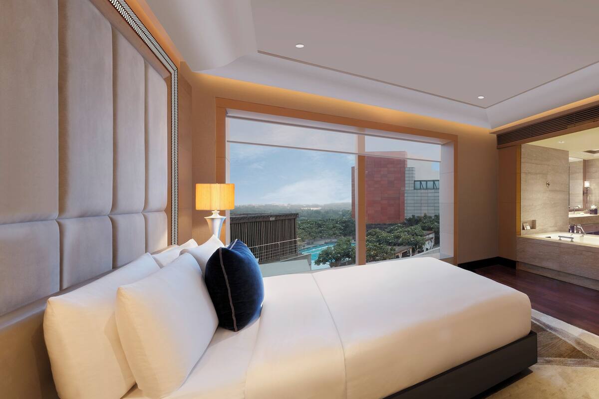 Habitación de hotel moderna con una cama grande, vistas a la ciudad, un baño independiente con bañera y un área de comedor.