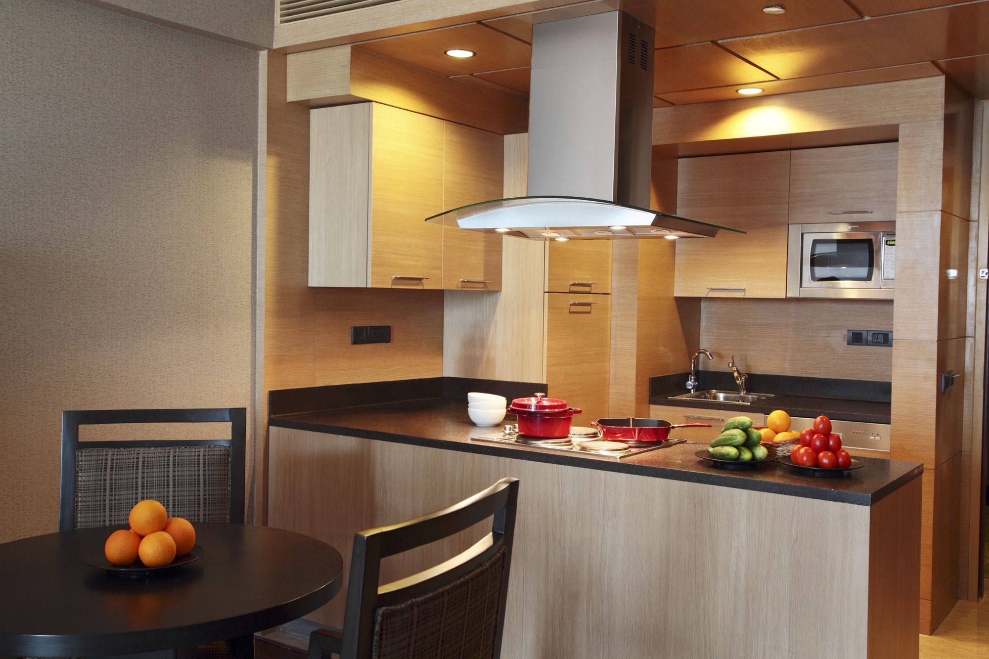 Cozinha moderna com armários de madeira, uma ilha central com frutas, micro-ondas e forno embutido.