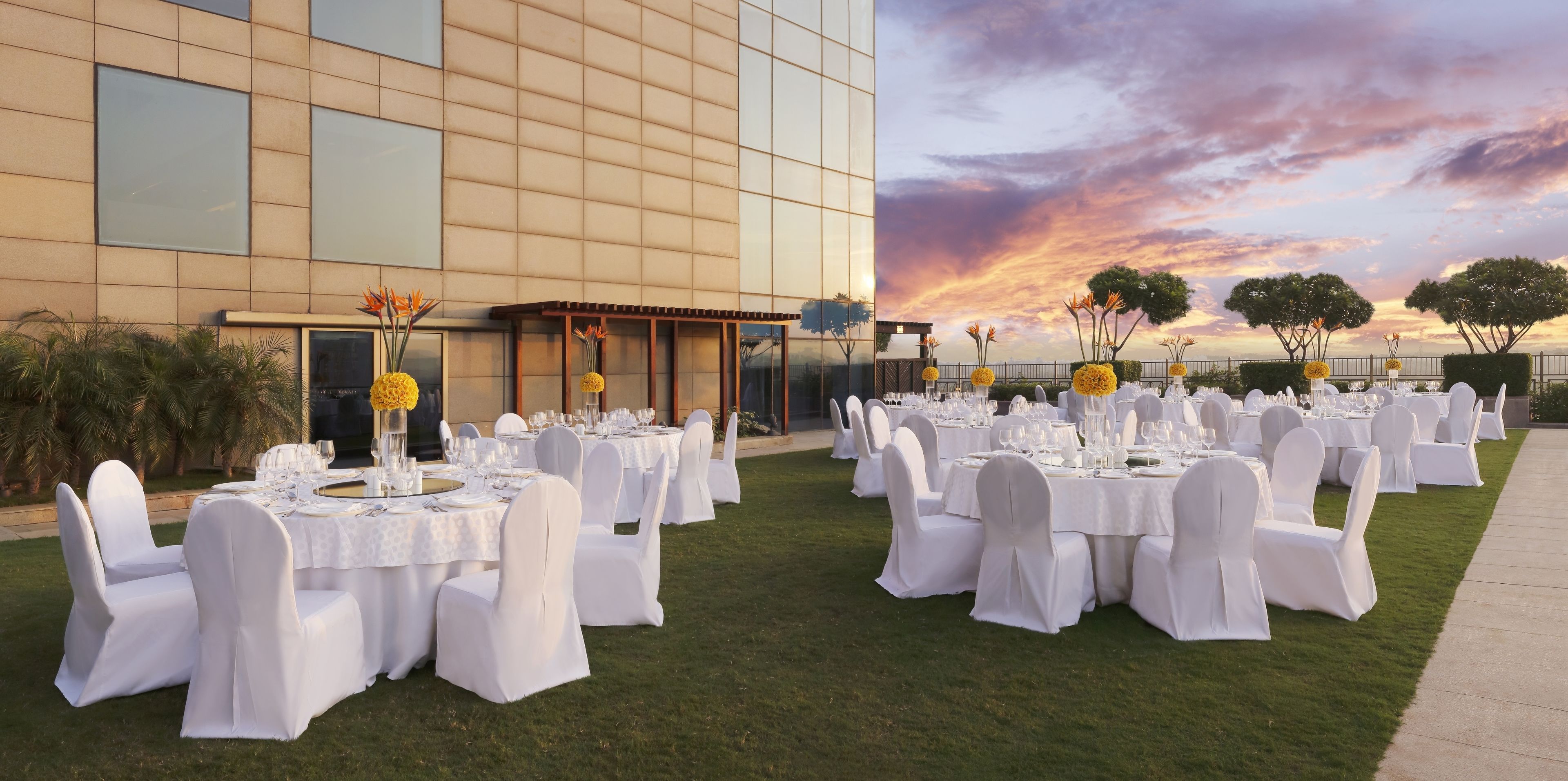 An outdoor banquet setup with tables and chairs, a building in the background, and a sunset sky.
