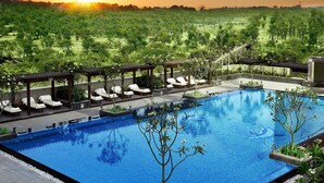 A swimming pool with lounge chairs and a view of the sunset over a green landscape. - The Leela Ambience Gurugram Hotel & Residences - The Luxury Urban Sanctuary (Gurugram)