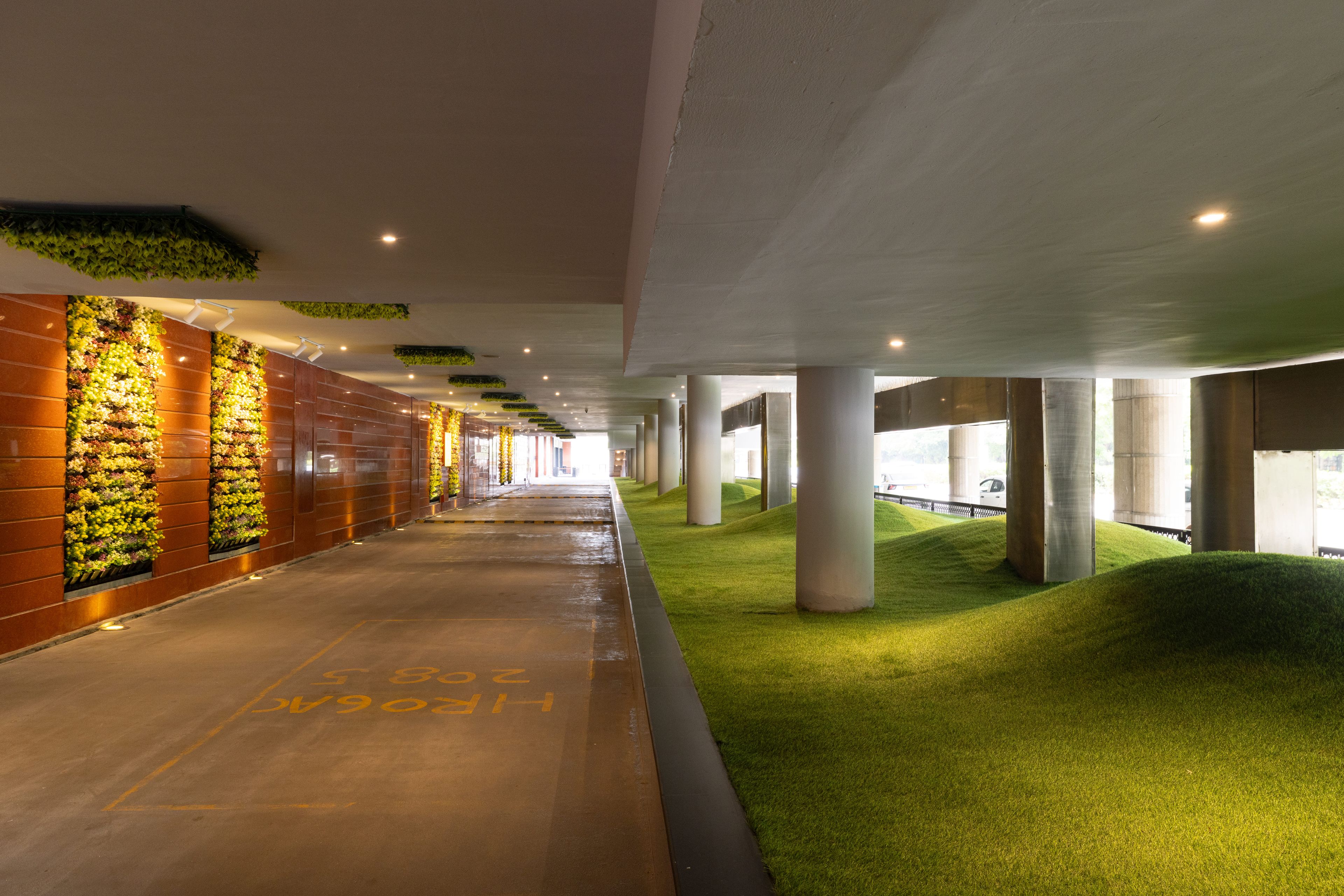 Un pasillo con zona de césped artificial verde, columnas y una pared con jardines verticales.