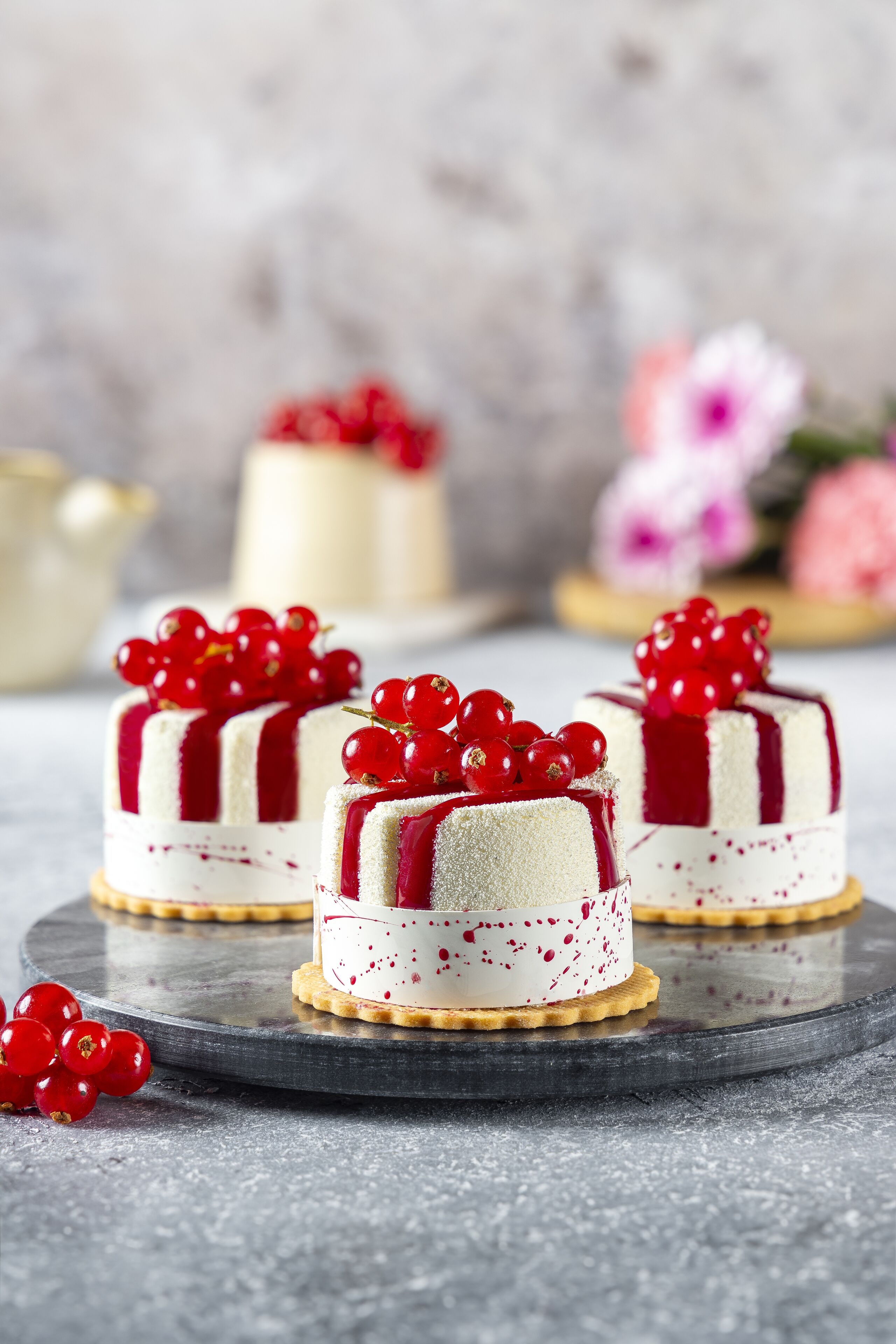 Three small cakes with red berries on a round table.