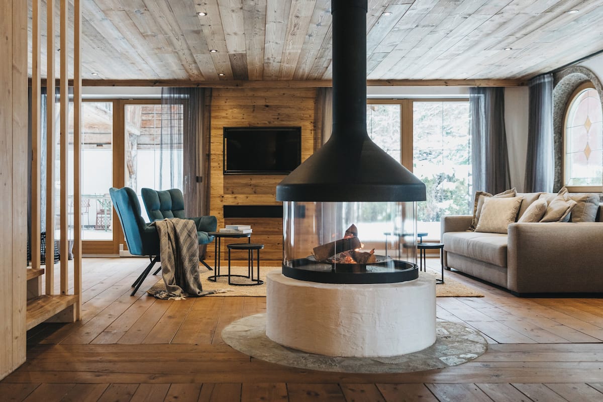 A cozy living room with a fireplace, wooden floors, a sofa, and a TV mounted on the wall.