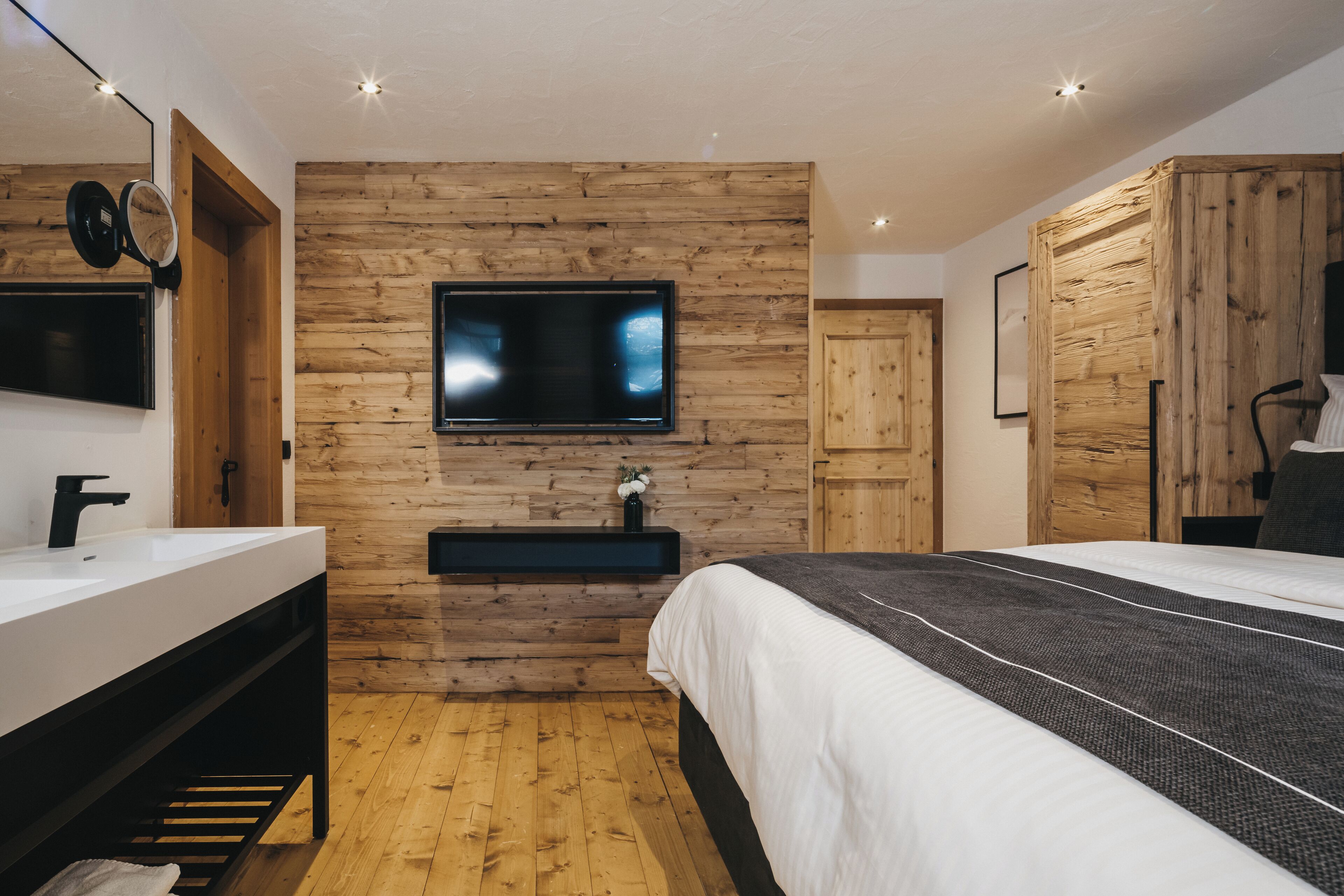 A modern bedroom with a wooden wall panel, a flat-screen TV, a bedside table, a bed, and a built-in bench.