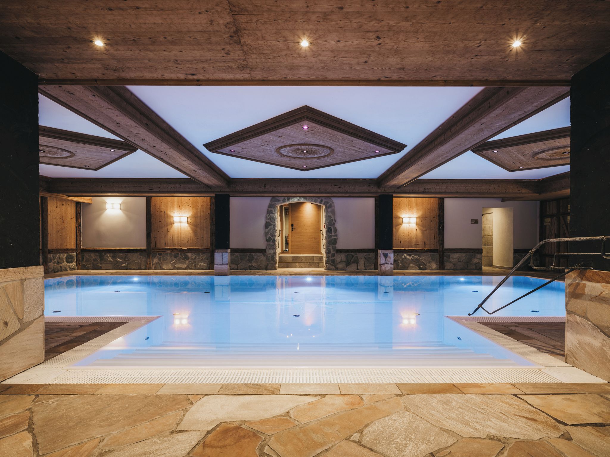 Una piscina interior con suelo de piedra, vigas de madera y paredes de piedra.
