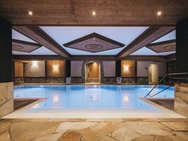 An indoor swimming pool with stone flooring, wooden beams, and stone walls.
