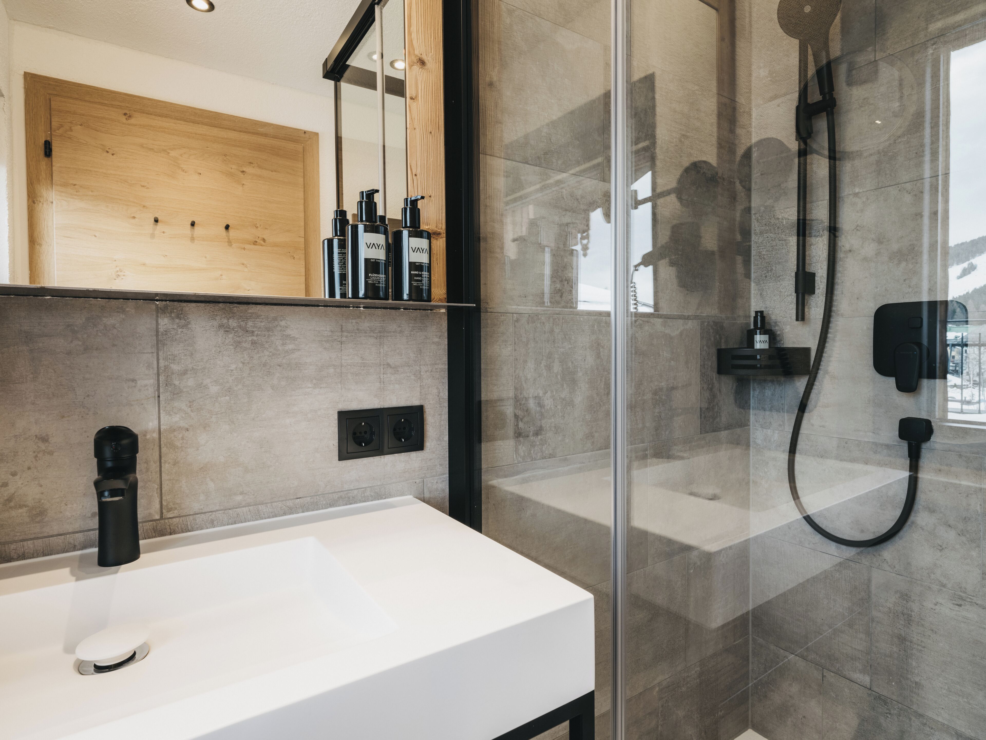 A modern bathroom with a white sink, a glass shower enclosure, and a wooden vanity.