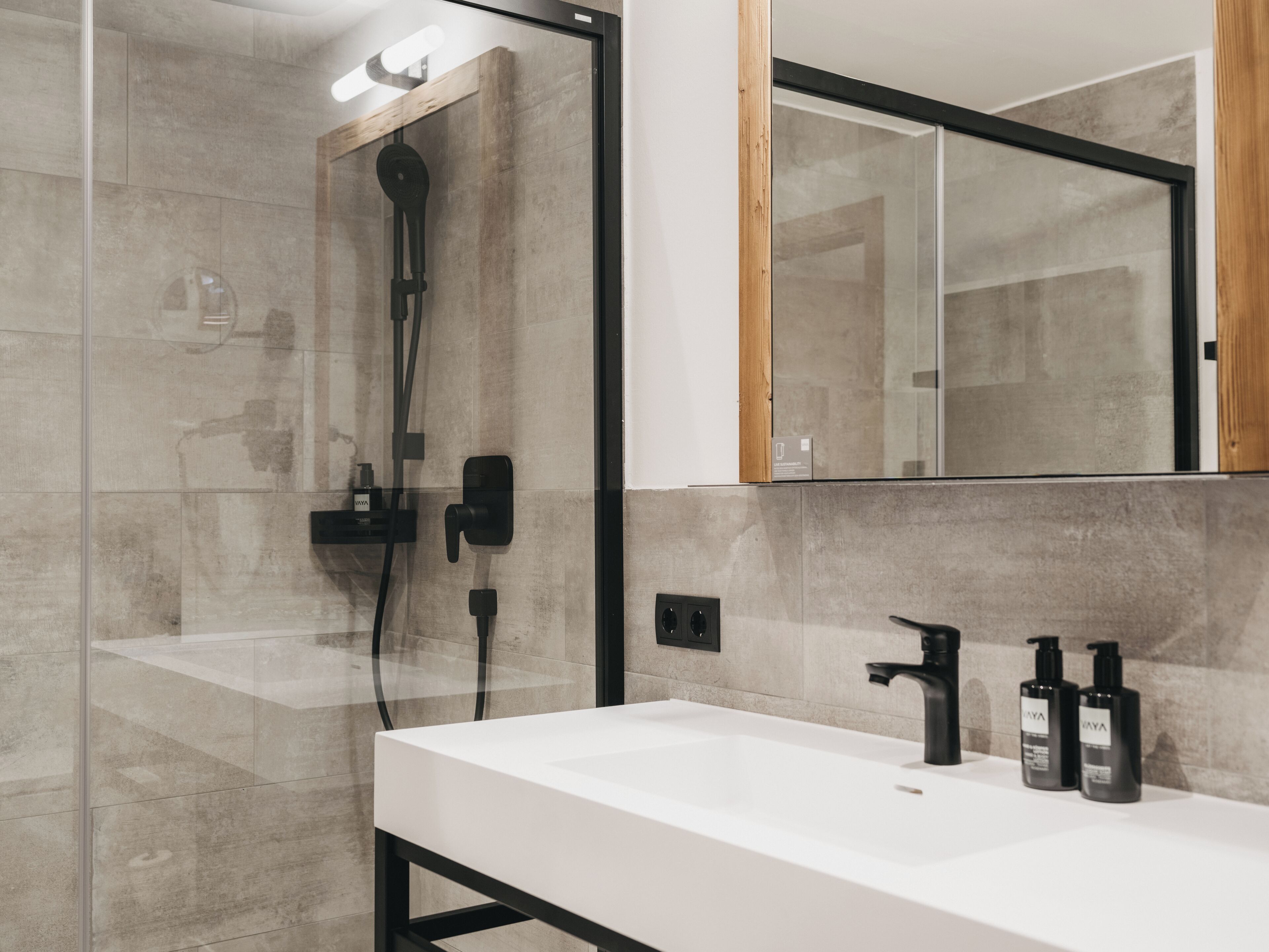 A modern bathroom with a glass shower enclosure, a white sink with black faucets, and a mirror above the sink.