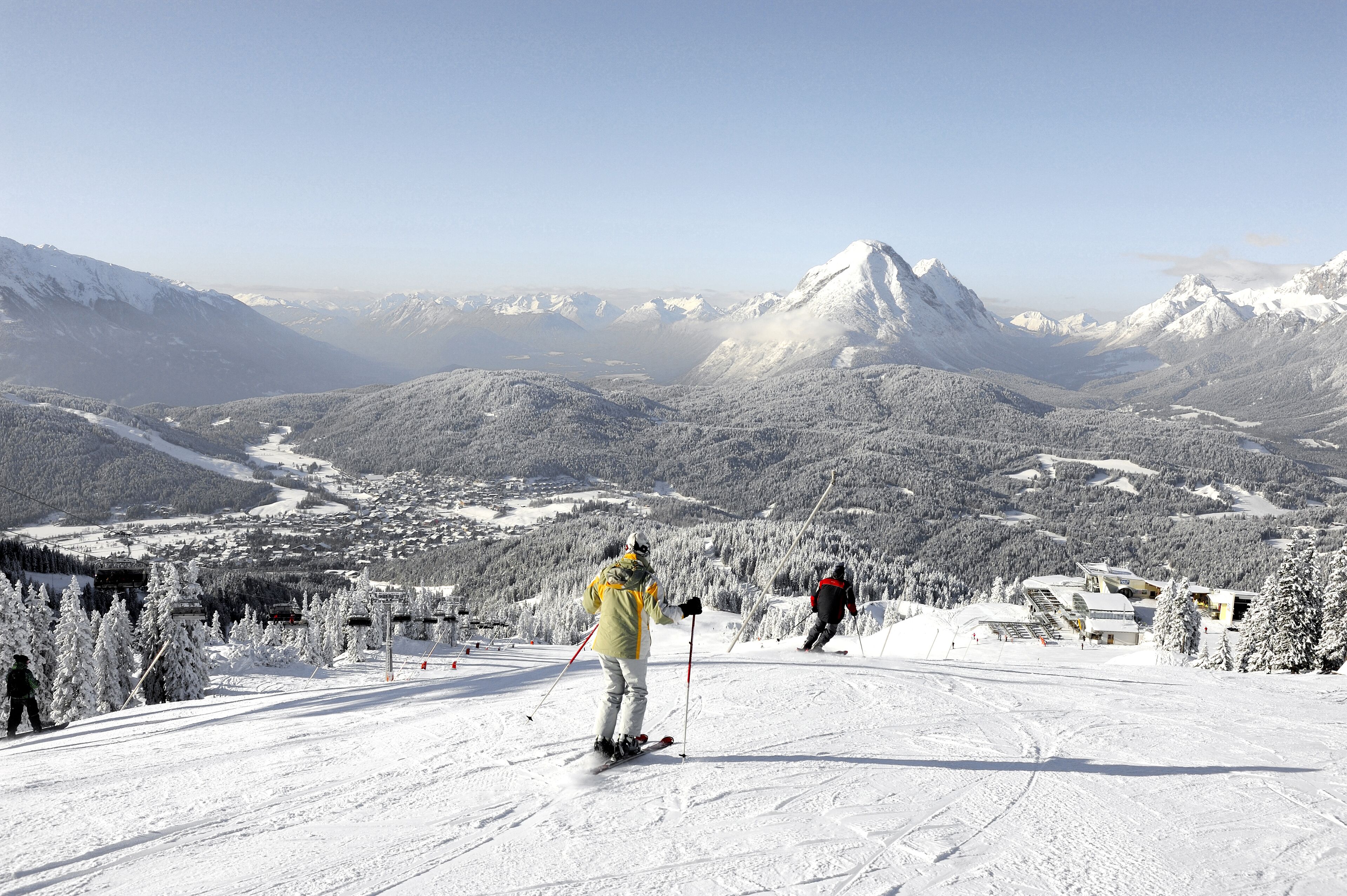 A snowy mountain landscape with skiers, a ski lift, and a ski resort building.