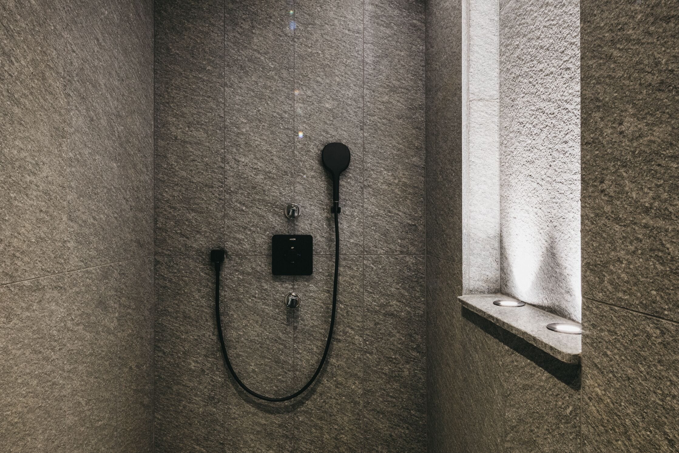 A shower with a control panel and a handheld showerhead mounted on a textured wall.