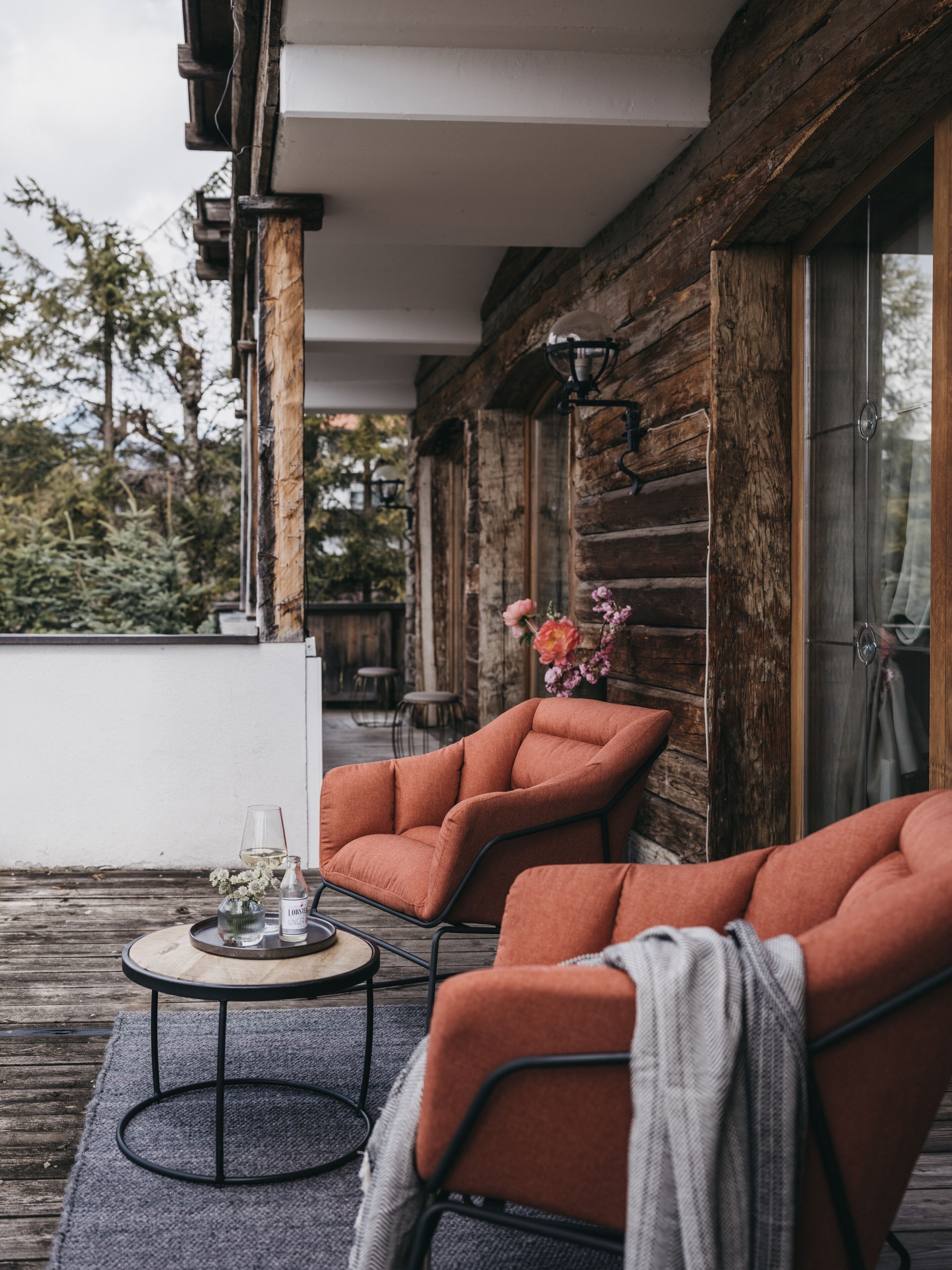 A wooden deck with two orange chairs and a small round table, a bottle of wine, and a glass.