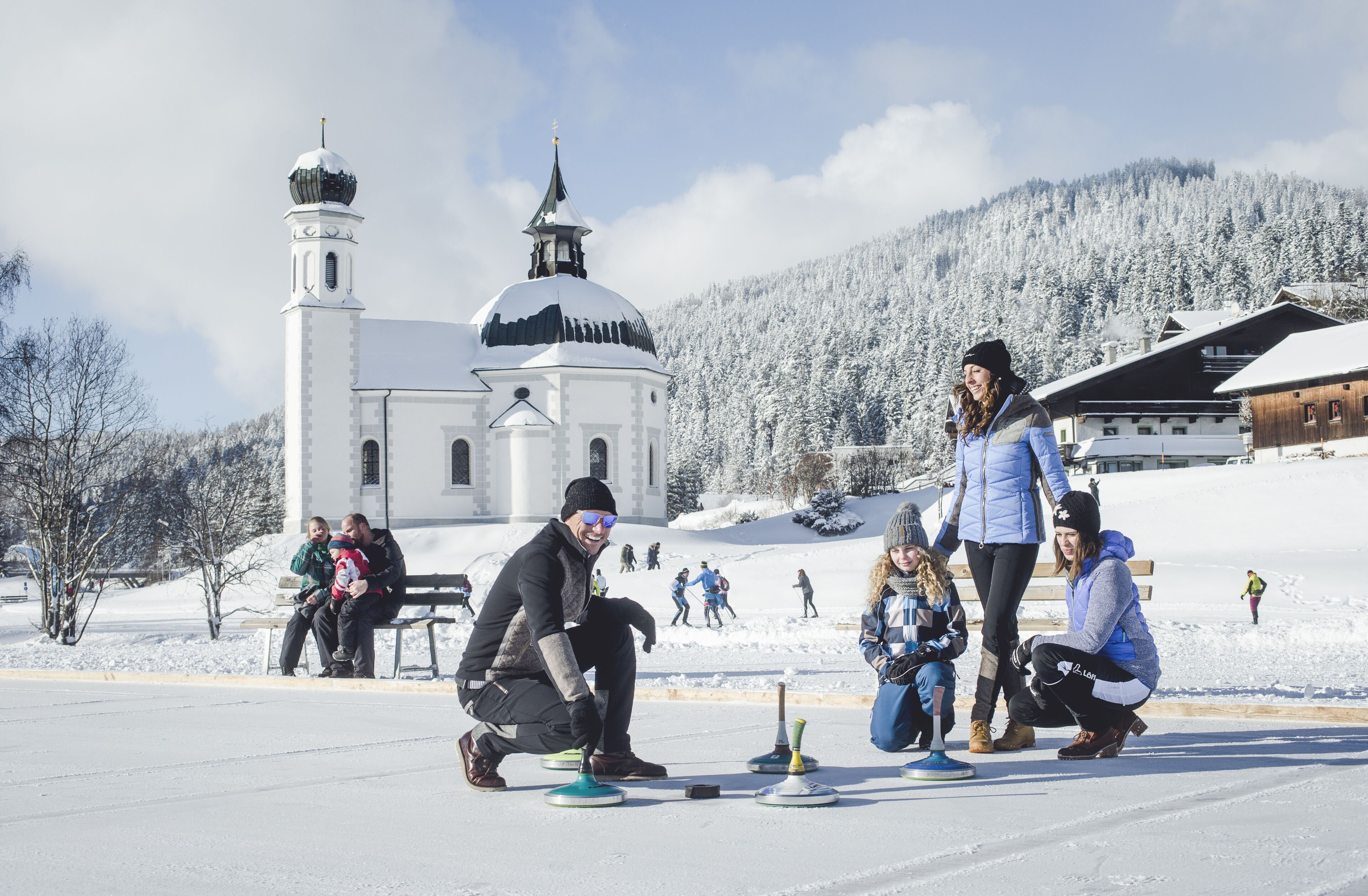 A snowy outdoor area with a church, benches, and people engaging in activities.