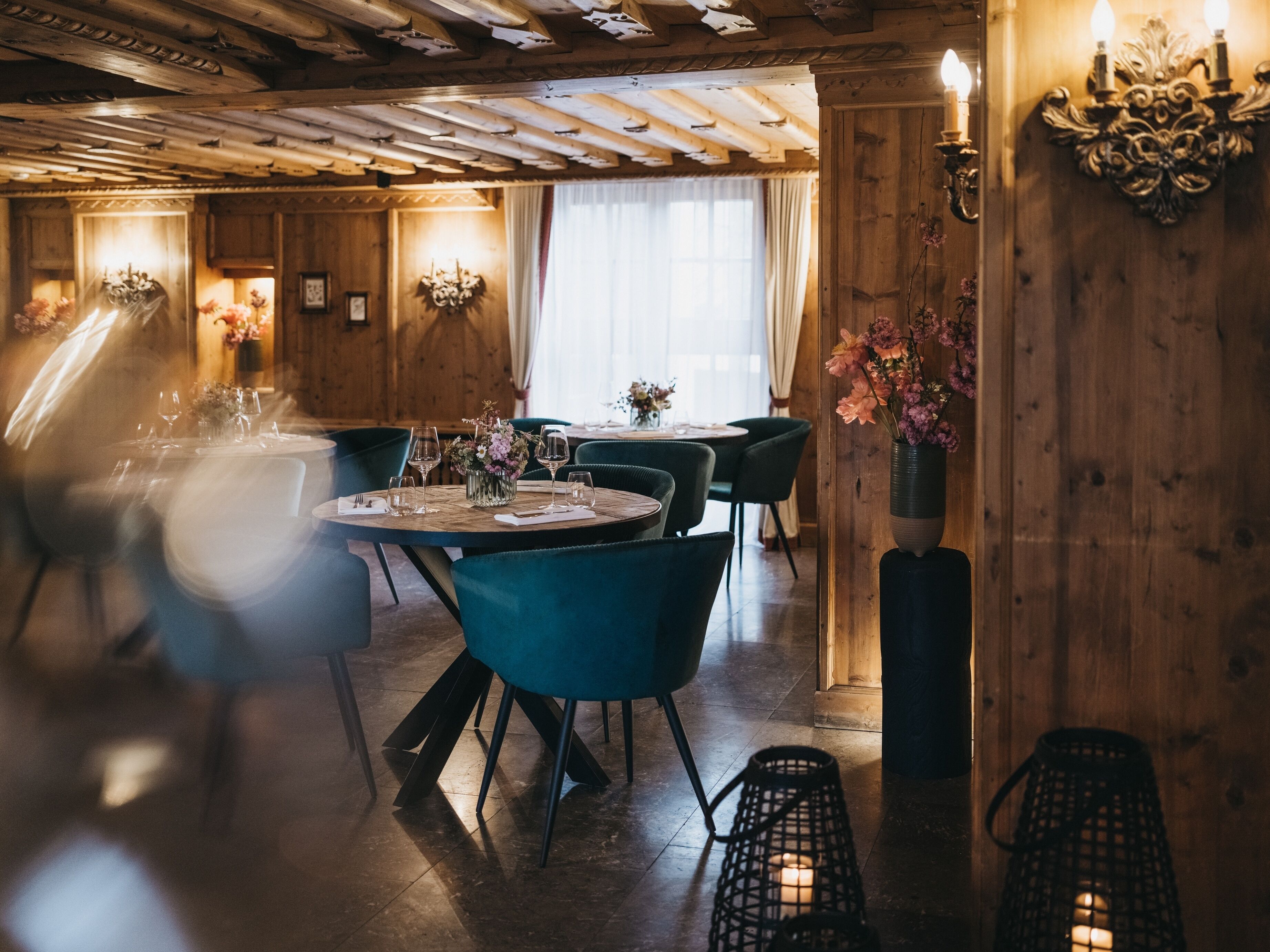Un restaurant aux murs et au plafond en bois, avec des tables rondes et des chaises, et des compositions florales en guise de décoration centrale.
