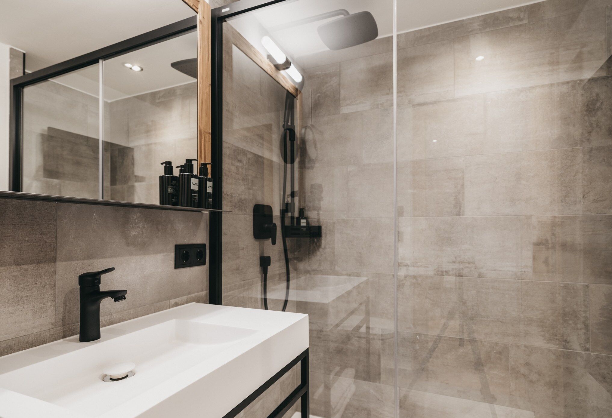 A modern bathroom with a white sink, black faucet, and a glass shower enclosure.