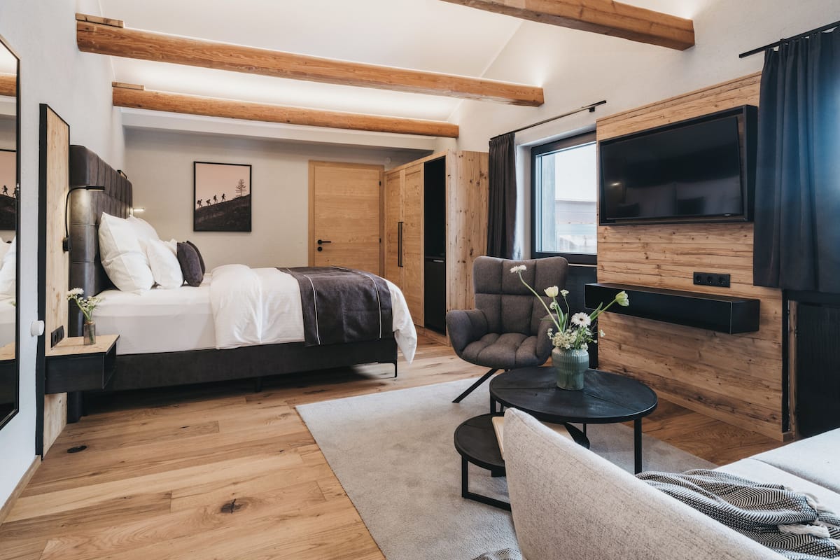 A modern bedroom with a bed, a chair, a TV, and a wooden ceiling.