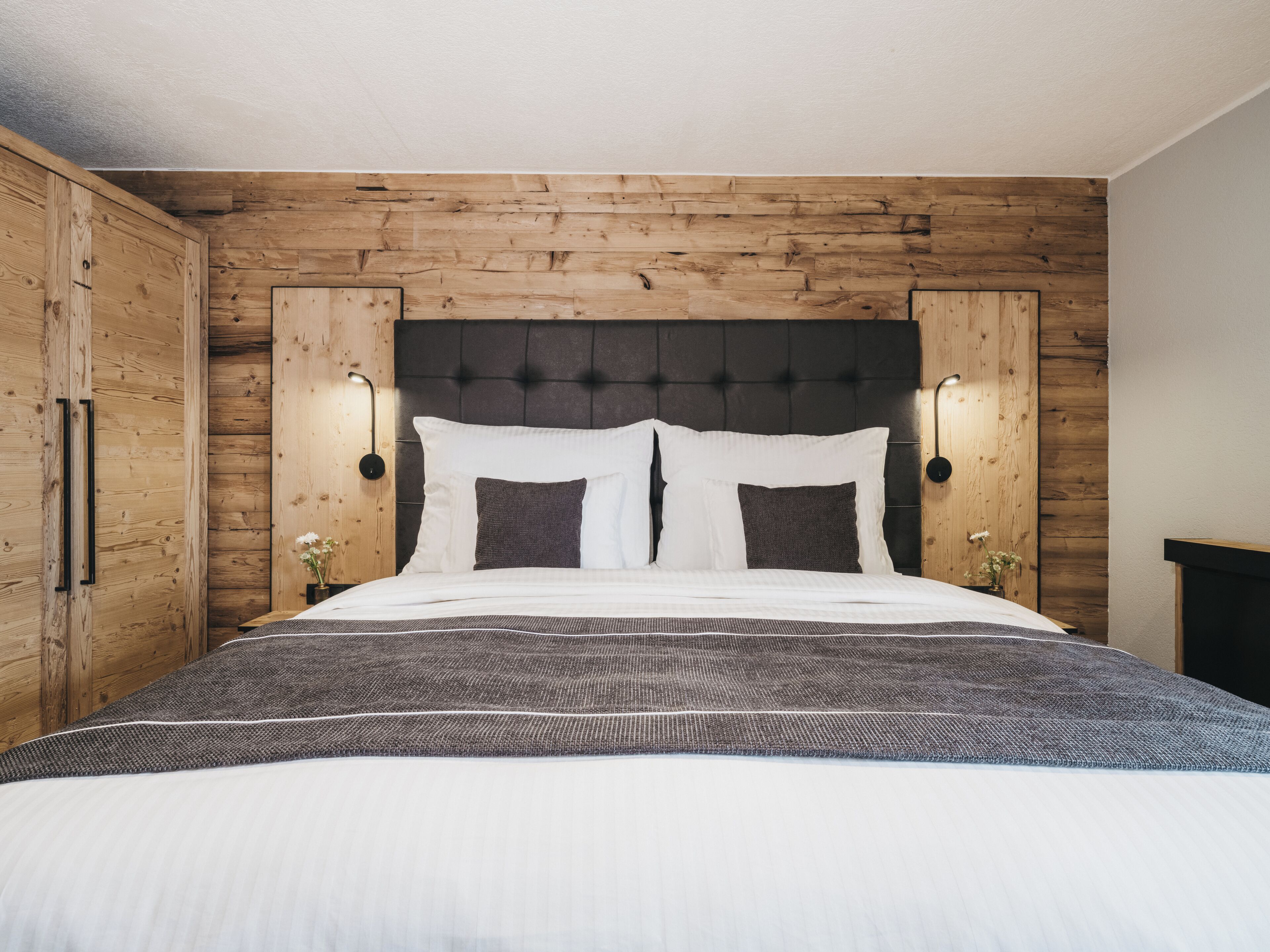 Een slaapkamer met een houten hoofdbord, twee bedlampjes en een bed met wit beddengoed.