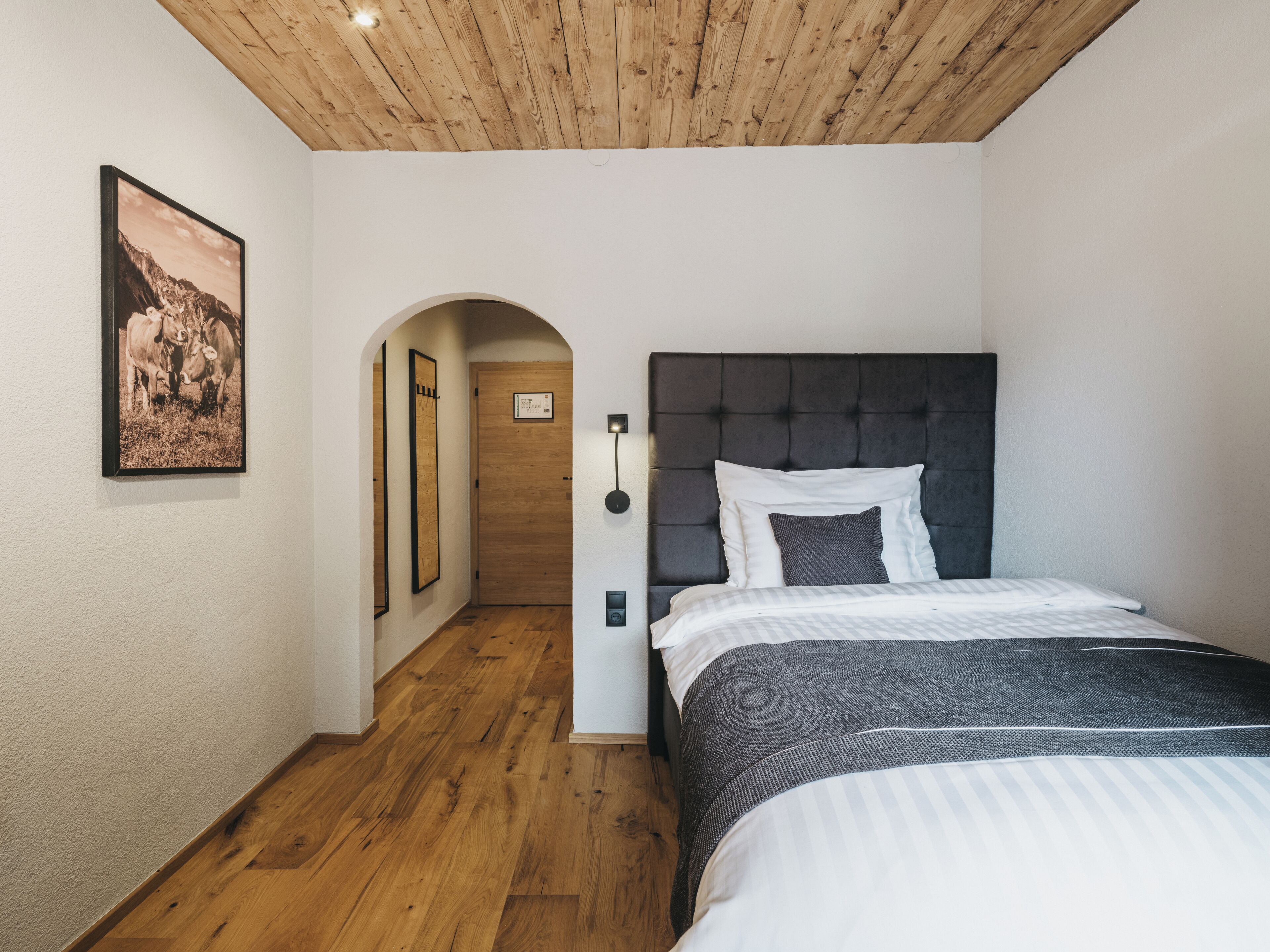 Un dormitorio con una cama, techo de madera, un cuadro enmarcado en la pared y un pasillo que conduce a otra habitación.