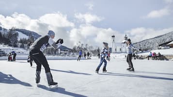 Een groep mensen schaatst over een met sneeuw bedekte ondergrond, met een kerk en bergen op de achtergrond.