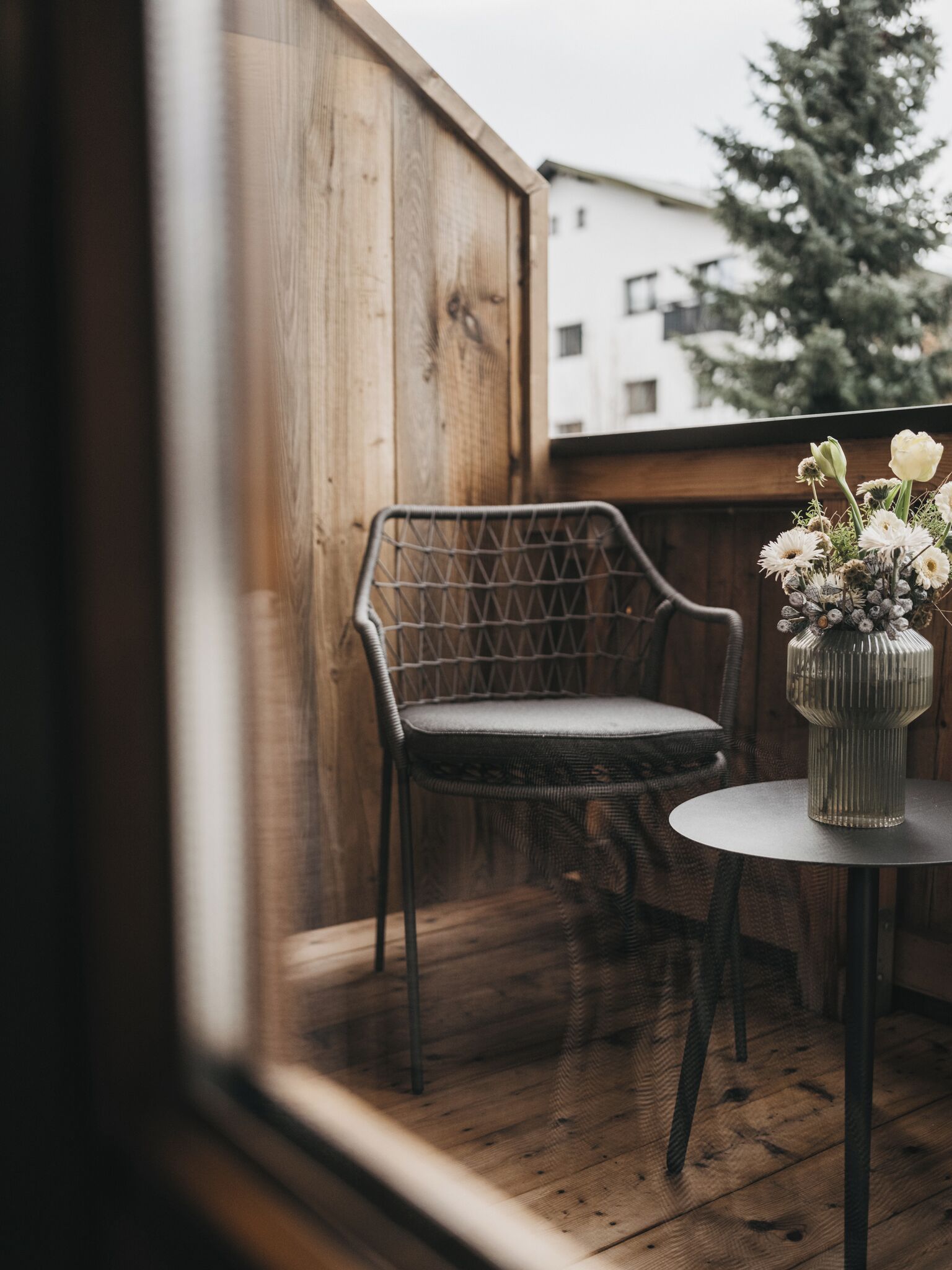 A wooden deck with a wicker chair and a small table with a vase of flowers.