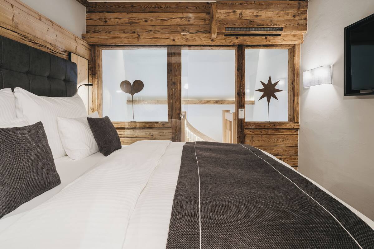 A bedroom with a large bed, wooden ceiling beams, a view of the outdoors, and a star decoration on the wall.