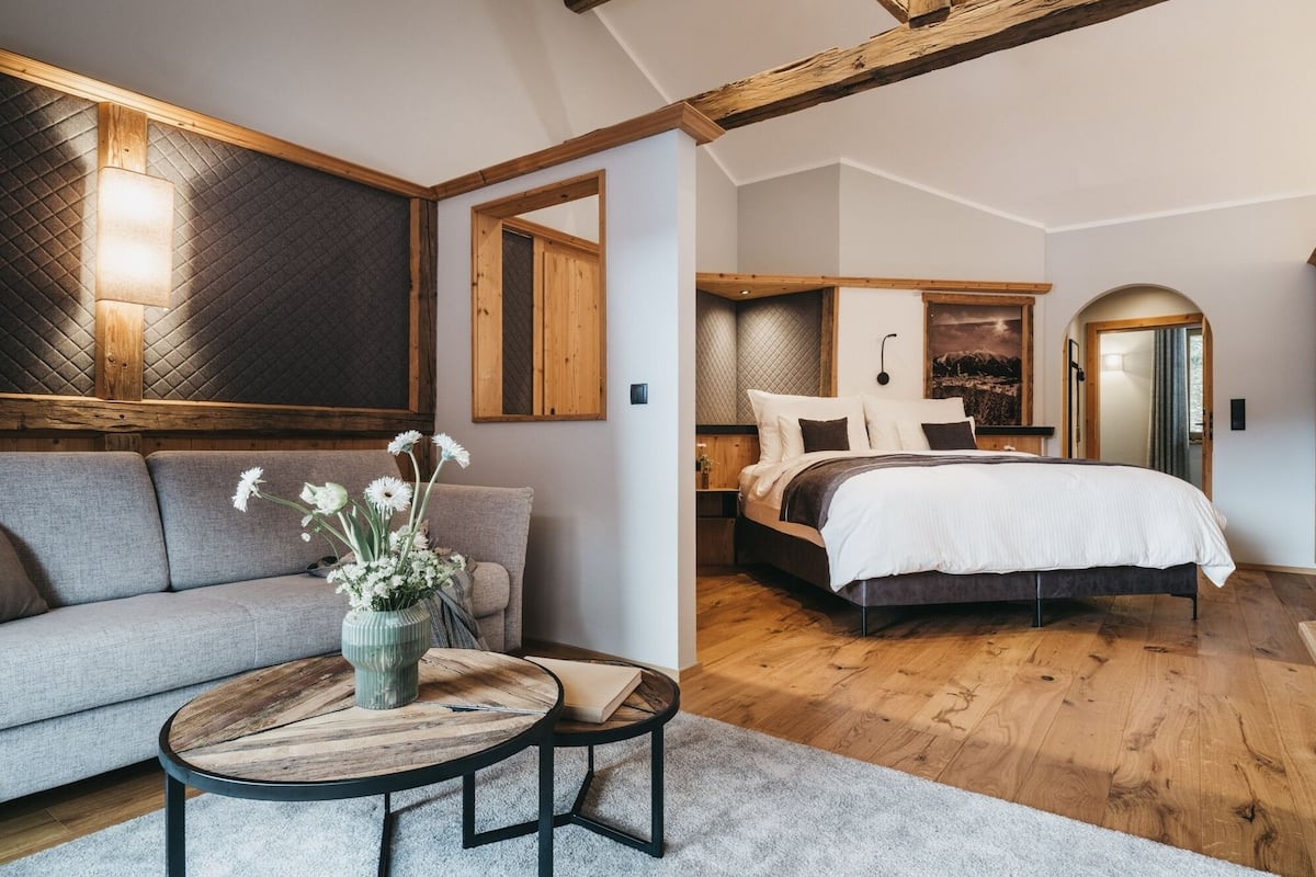 A modern bedroom with a wooden ceiling, a large bed, a sofa, and a small table with a vase of flowers.