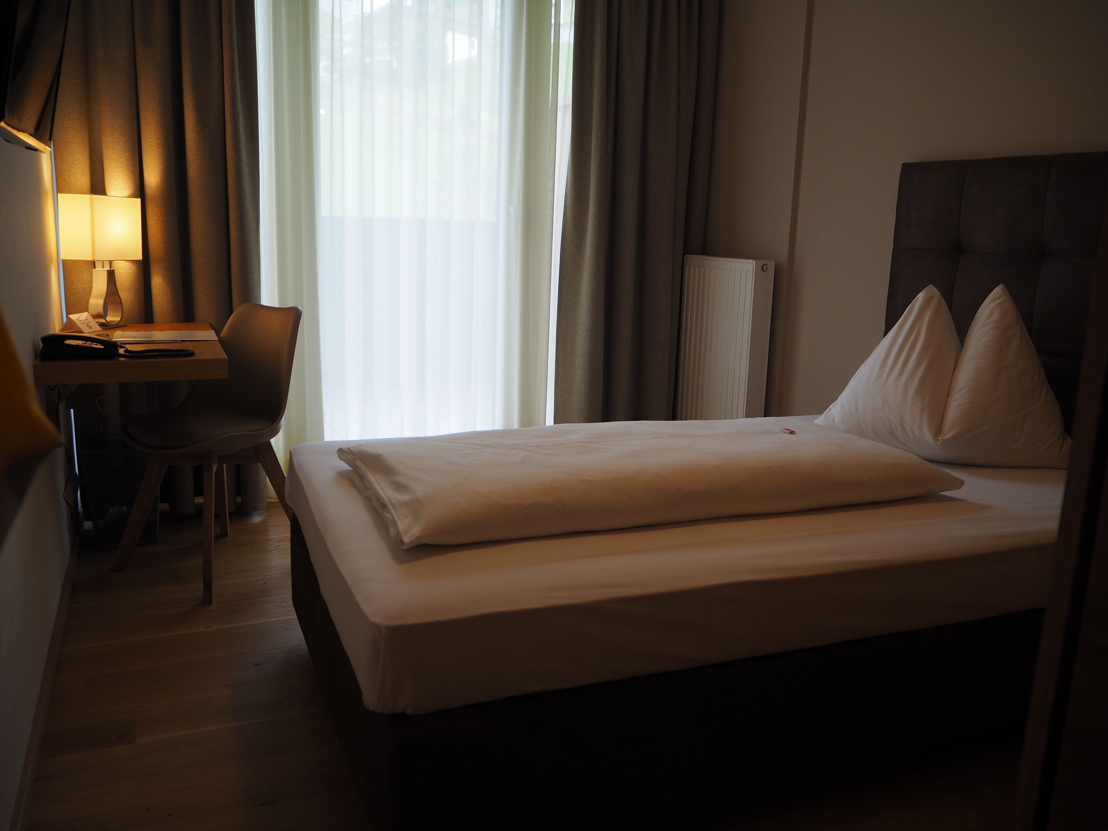 Een hotelkamer met een bed, een bureau, een stoel en een lamp.