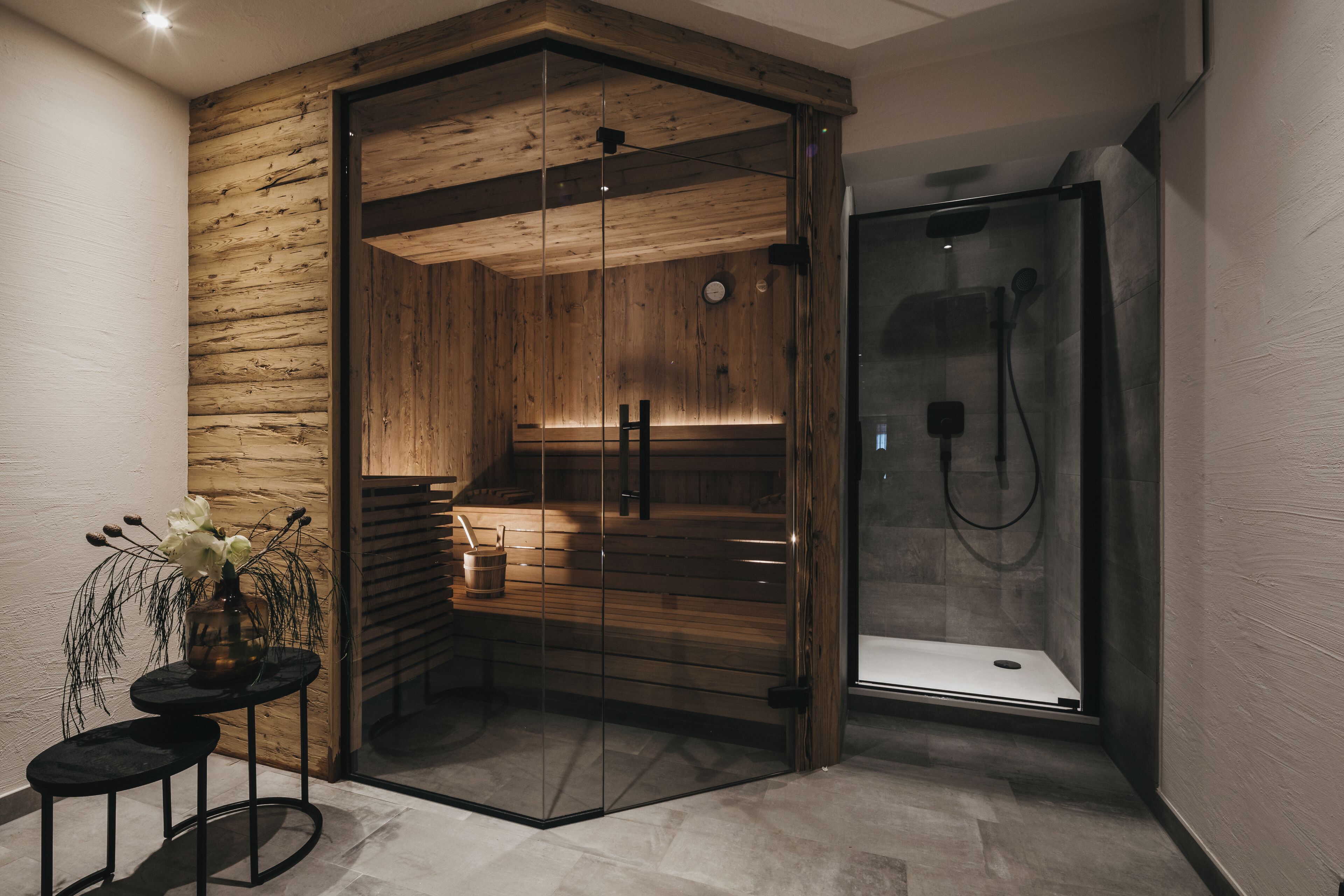 Un bagno moderno con sauna in legno, cabina doccia in vetro e un piccolo tavolo con un vaso di fiori.