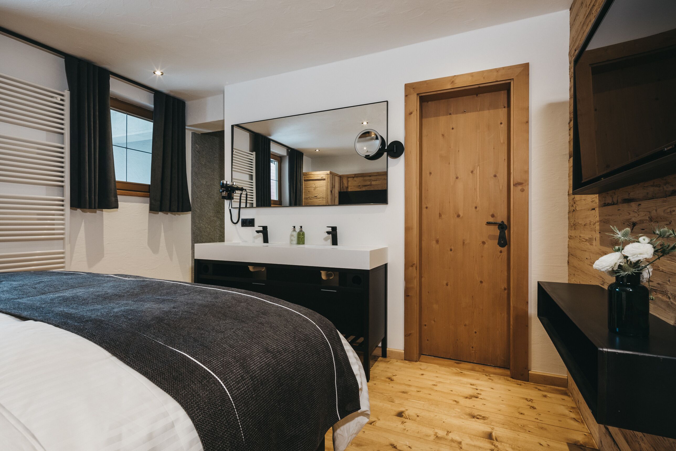 Une chambre à coucher avec un lit, une porte en bois, un mur blanc, un miroir et une commode noire.
